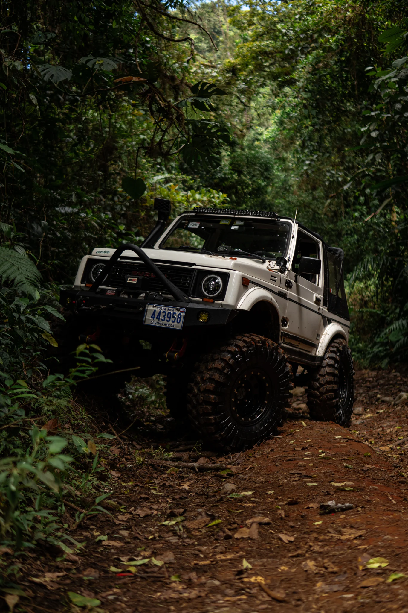 White Suzuki Samurai navigating a rocky off-road trail in the forest