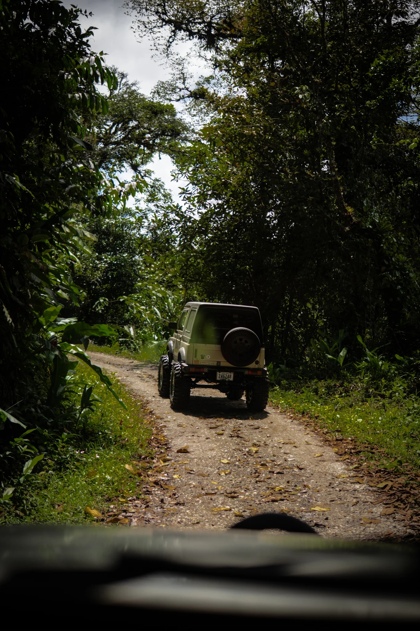 Suzuki Samurai driving away along a sunlit forest road in Costa Rica