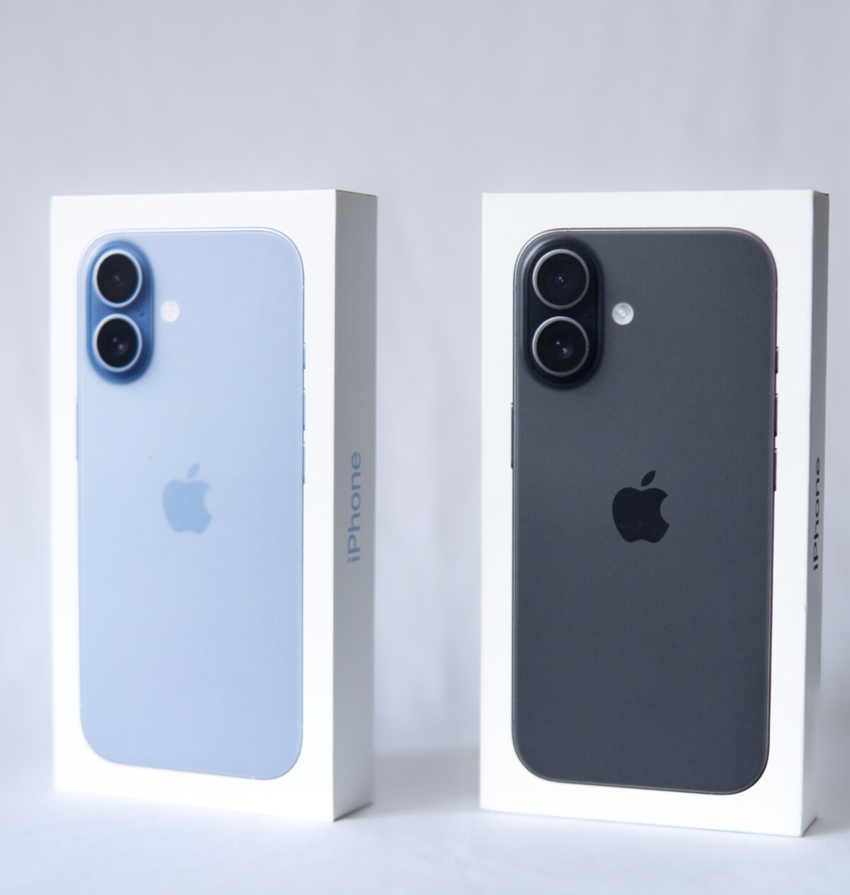 Two iPhone boxes with blue and black iPhones on a white background