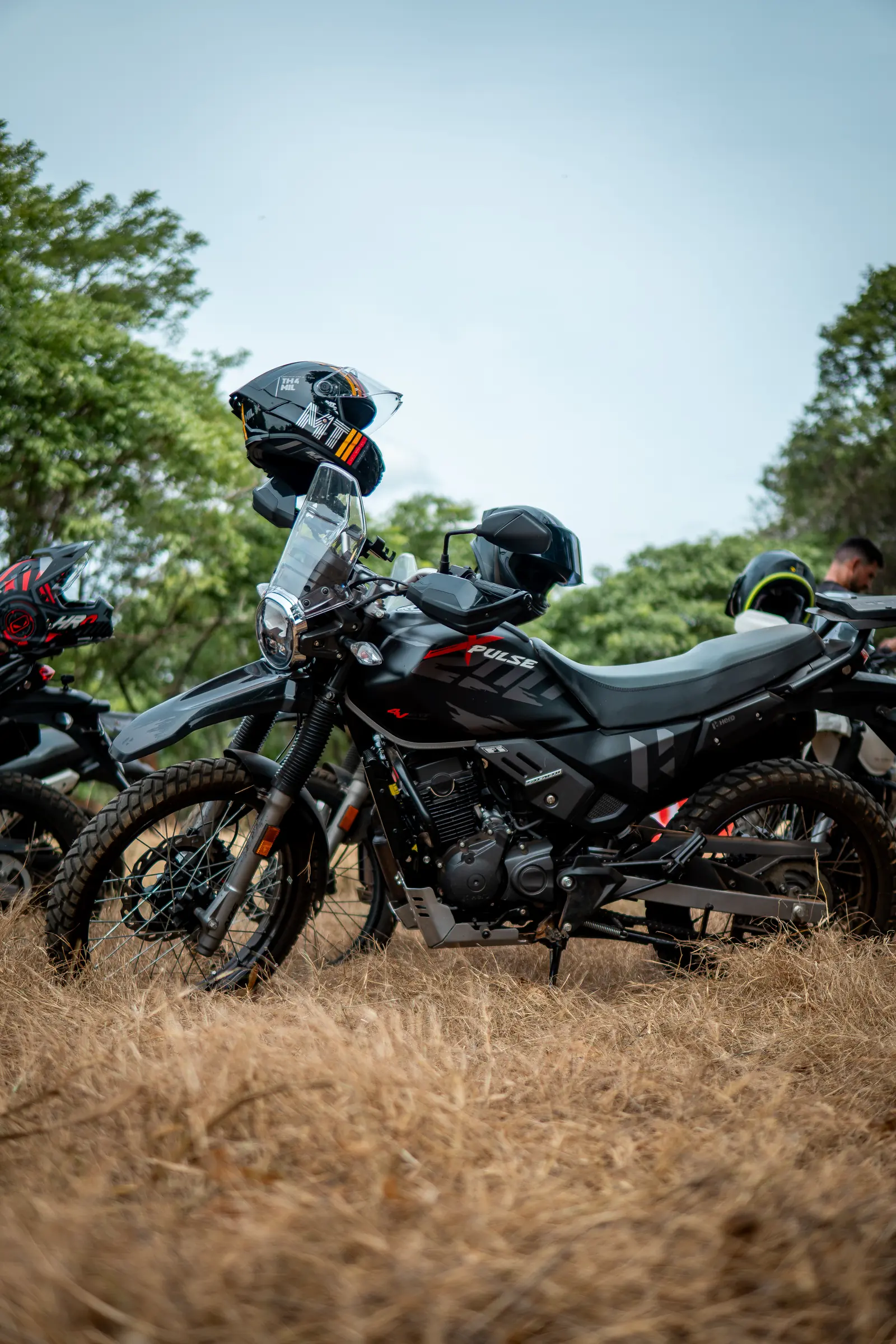 Black motorcycle parked in dry grass with helmets resting on it